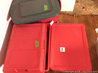 Two red plastic storage bins with lids, one gray, all labeled with lot numbers.