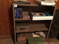 Metal bookshelf with multiple items on three shelves in a basement setting.