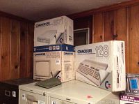 Three boxed Commodore items: 1571 disk drive on top of 1902A monitor box, next to 128 computer box