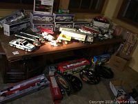 Overview of assorted toy trucks on table and boxed sets against wall