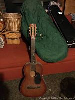 Full view of acoustic guitar on couch with green soft case behind