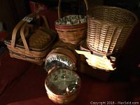 Photo showing six Longaberger baskets and one plant pot size basket grouped together, some featuring floral fabric liners, displaying natural wood material and woven craftsmanship.