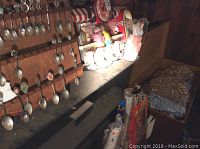 Photo of a wooden chest filled with black cedar shavings and a collection of silver souvenir spoons hanging on the lid.
