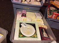 Bins containing more than 30 boxed Precious Moments figurines showing a variety of boxed designs and sizes arranged in storage bins.