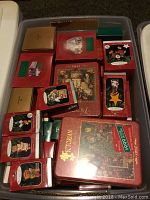 Plastic bin filled with multiple red and green Hallmark Keepsake ornament boxes and two large red puzzle tins