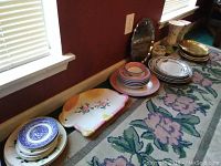 Photo showing various stacks of plates, a ceramic platter with floral design, and a silver-plated serving tray