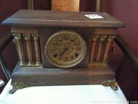 Full view of the vintage wooden mantel clock showing wooden columns with gold accents and the face of the clock.