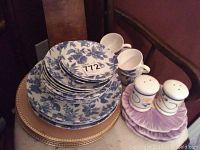 Blue and white floral patterned plates and cups stacked on gold charger plates with salt and pepper shakers on a pink ceramic tray nearby.