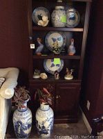 Front view of the dark wooden shelf with blue and white plates displaying apple and pear designs, blue and white bird and duck figurines in front, and smaller jars on the bottom shelves.