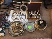 Photo showing the overall collection of silver-plated and pewter trays, flatware, and utensils spread on carpet