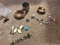 Photo showing collection of costume jewelry on carpet including charm bracelets, rings, clip-on earrings, and watch