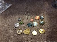 Overview of all costume jewelry pendants and one necklace displayed on carpet including various cameo designs, gold-tone pendants and floral motif pieces