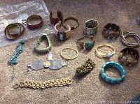 Overview image showing different bracelets including bangles, cuffs, and stretch bracelets in various metal tones and colors placed on a carpeted surface.