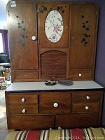 Front view of cabinet showing enameled countertop, wood drawers with ceramic knobs, painted floral center panel