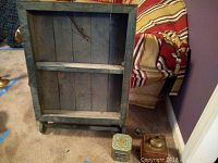 Wooden shelf with visible legs and two shelves, distressed green paint with wear marks. Manual coffee grinder and decorative tin placed beside it on carpet.