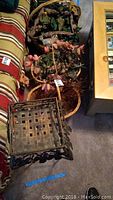 Four large items including three wicker baskets with artificial flowers and one black metal plant stand. The baskets contain pink and green artificial floral arrangements.