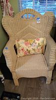 Front view of one off white wicker chair with a floral accent pillow on the seat.
