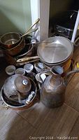 Copper pans, pots, metal pitcher, teapot, and small bowls arranged on floor