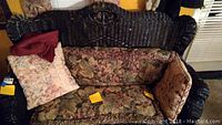Full view of black wicker love seat with floral tapestry cushions and pillows, showing overall design and colors.