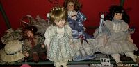 Four porcelain dolls dressed in detailed vintage clothing displayed on a shelf