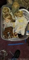 Plastic tub containing 6 dolls, including porcelain and rag dolls, and some small items including doll parts and miniature furniture pieces