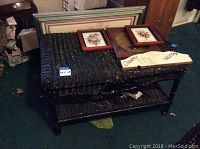 Overall view of the painted black wicker table holding framed artwork and wooden signs, showing wear and scratches.