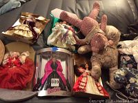 Photo showing five holiday Barbie dolls in various festive outfits and four floral fabric stuffed bears together on couch.