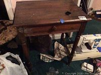 Wooden side table visible from the front showing drawer and turned legs. Tabletop has surface wear and a split down the center.
