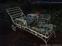 Photo showing white metal lounger with floral cushions and glass top table outside on patio with signs of rust and wear.