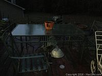 Image showing the outdoor green metal table with glass top and one of the matching chairs on wooden deck at dusk.