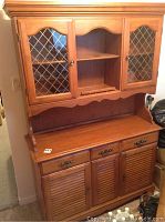 Full view of the wooden hutch showing upper glass cabinet doors with diamond-shaped patterns, open center shelf, and closed lower cabinet with drawers and doors.