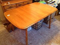 Full view of wooden dining table with leaf attached, showing honey wood finish and turned legs.