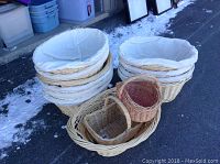 Photo showing a grouping of large, round wicker baskets with white fabric liners stacked together and various smaller wicker baskets in front including oval and elongated shapes.