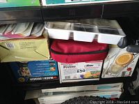 Shelf with boxed Black & Decker 3.8L pressure cooker, 16-piece beverage glass set, white ice cube tray, and boxed 10-speed blender with glass pitcher and orange infuser.