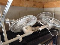 Three white Home Styles fans stacked and leaning, with visible power cords and mounting poles.