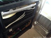 Photo of black shelving unit holding various household items such as a circular metal tray and other objects.