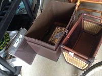 Three containers including two foldable brown faux leather storage organizers and one woven bamboo-style decorative basket with fabric lining, placed on floor near other household items.