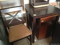 Photo showing one dark wooden chair with cross-back design next to the dark wooden square table in storage setting.
