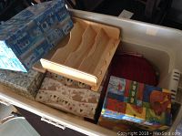 Photo showing mix of small decorative boxes, wooden segmented tray, and additional boxes inside a white tote bin.