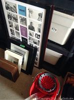 Several picture frames in black, white, and brown colors stacked upright against white plastic storage bins. Large red umbrella and tan tote bag visible.