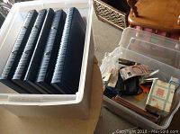 Plastic bin with five black and blue striped accordion file folders inside, and adjacent plastic container holding miscellaneous office items including notebooks and envelopes.