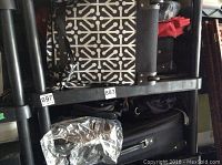 Shelf with black softshell suitcase, black and white patterned cooler, black hard-shell suitcase, silver insulated bag