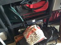 Photo showing variety of suitcases, including black hard-shell, red and black duffel bags, and leopard print bag on top of other bags.