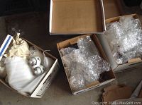 Wide view showing three boxes with various wrapped ceramic and glass items including jugs and containers.