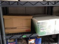 Plastic shelves with one cardboard box and one plastic bin labeled 889 containing dishes and kitchenware.