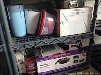 Shelf displaying blue and white ribbed pitchers or containers, plus packaged knives and kitchen tools