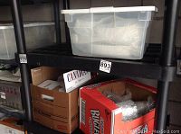 Plastic storage bin and cardboard boxes on black shelving in storage space.