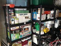 Photo showing fully assembled black plastic shelving units loaded with various boxed household items, indicating size and condition.