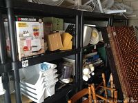 Wide view of shelving unit showing three shelves made of black molded plastic with various items on shelves (not included).