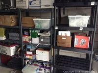 Three black plastic shelving units filled with boxes and storage containers in a storage area.